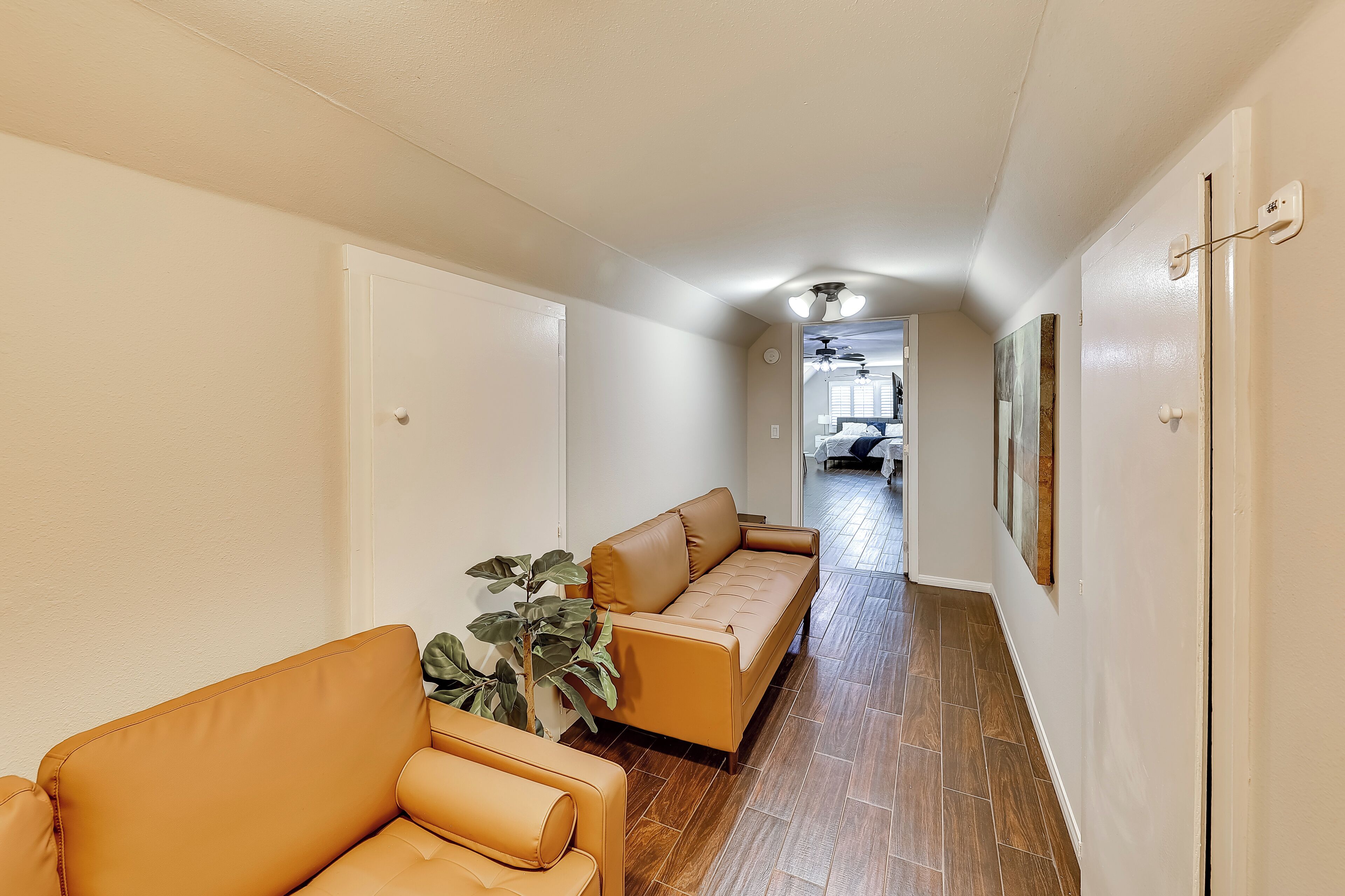 A hallway with a sofa and a plant, leading to a room with a ceiling fan.