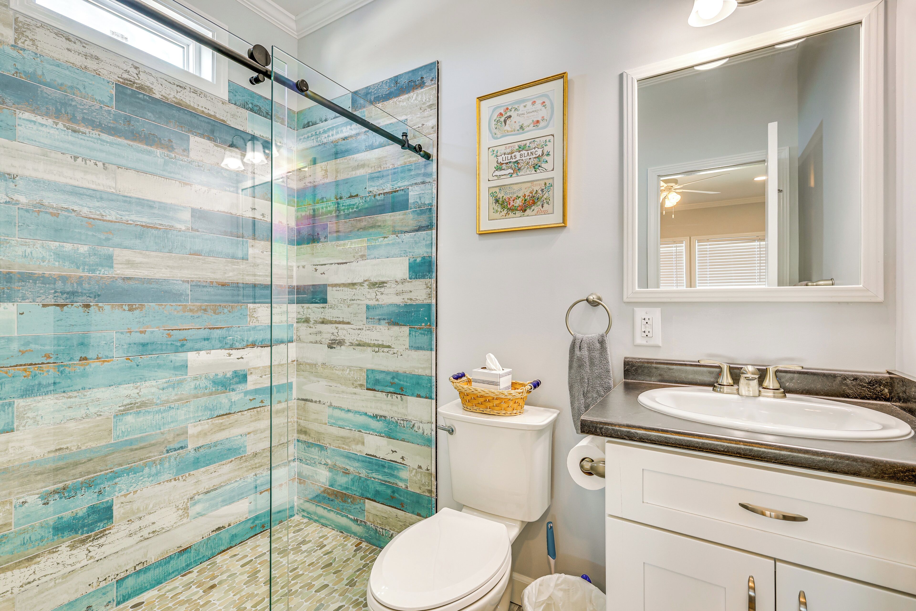 A bathroom with a glass shower enclosure, a white toilet, a sink with a marble countertop, and a mirror above the sink.