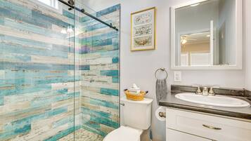A bathroom with a glass shower enclosure, a white toilet, a sink with a marble countertop, and a mirror above the sink.