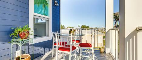 Un balcon avec une table et des chaises blanches, une plante en pot et une fenêtre avec des volets verts.