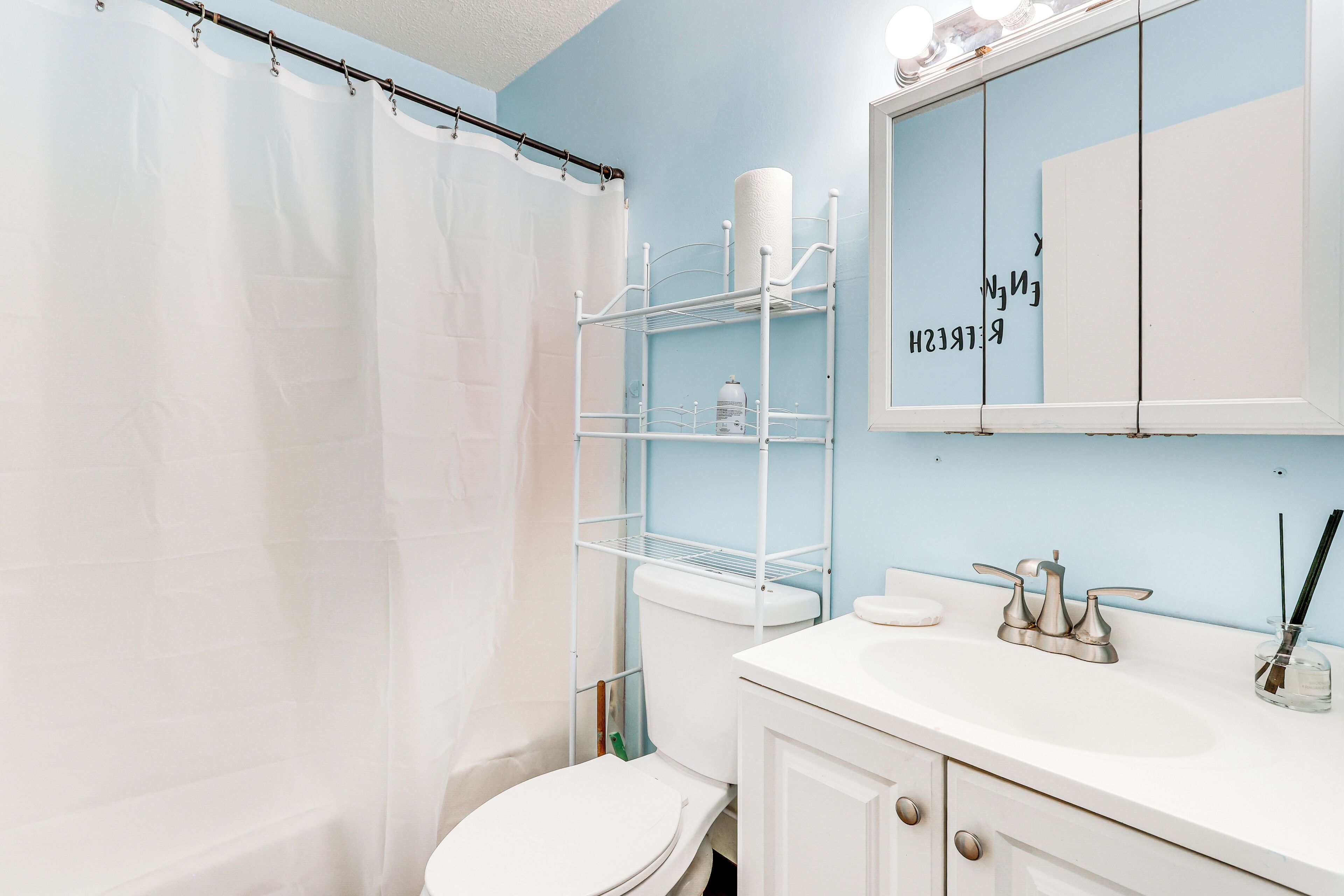 Une salle de bain avec des toilettes blanches, un lavabo blanc, un miroir et un rideau de douche.