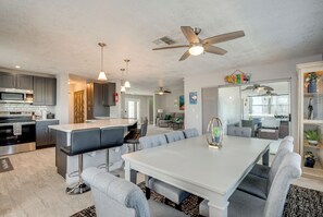 A modern kitchen with a central island, bar stools, and a dining area with a white table and grey chairs. - Canal & Gulf Views: Spacious Hudson Home (Hudson)