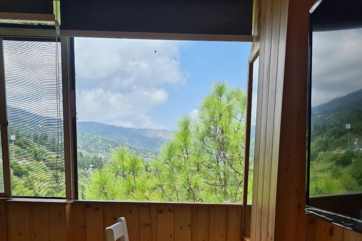 A wooden cabin room with a view of green hills and trees.