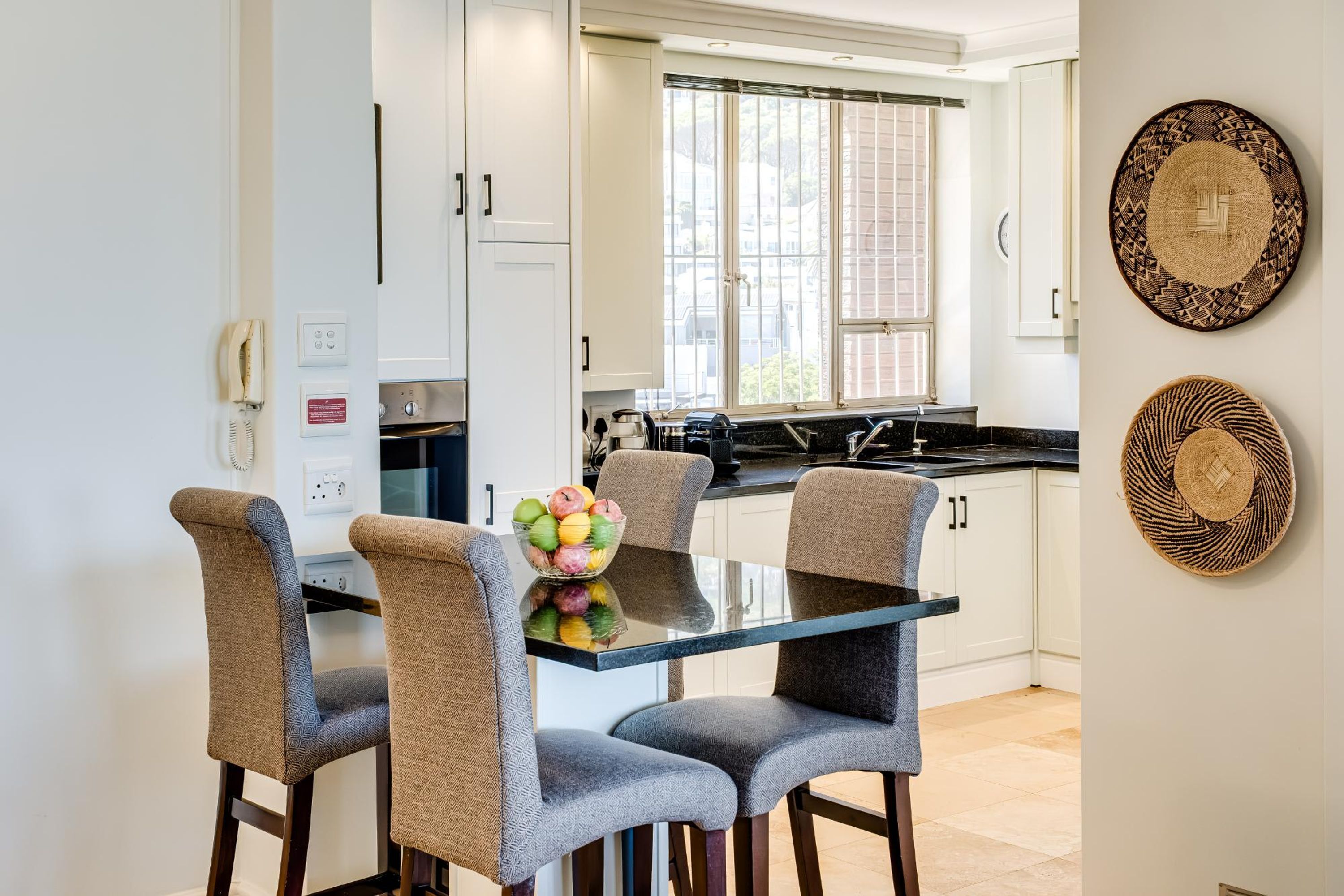 A modern kitchen with white cabinets, a black countertop, and a glass dining table with four chairs.