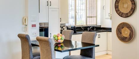 A modern kitchen with white cabinets, a black countertop, and a glass dining table with four chairs.