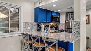 Eine Küche mit blauen Schränken, Granit Arbeitsplatten, einem Edelstahl-Kühlschrank und einer Bar mit Hockern.