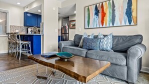 Ein modernes Wohnzimmer mit einem grauen Sofa, einem Holztisch und einem farbenfrohen abstrakten Gemälde.