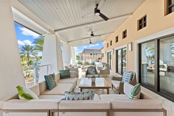 A covered outdoor seating area with sofas, chairs, and a ceiling fan.