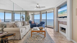 A spacious living room with a large window overlooking the ocean, a ceiling fan, a fireplace, and a cozy seating area with a coffee table. - ☀️Ebb Tide 806-Oceanfront with Fabulous Views-Pool+Hot Tub☀️ (New Smyrna Beach)