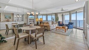 A spacious living area with a dining table, chairs, a sofa, and a coffee table. There is a large window providing a view of the ocean. - ☀️Ebb Tide 806-Oceanfront with Fabulous Views-Pool+Hot Tub☀️ (New Smyrna Beach)