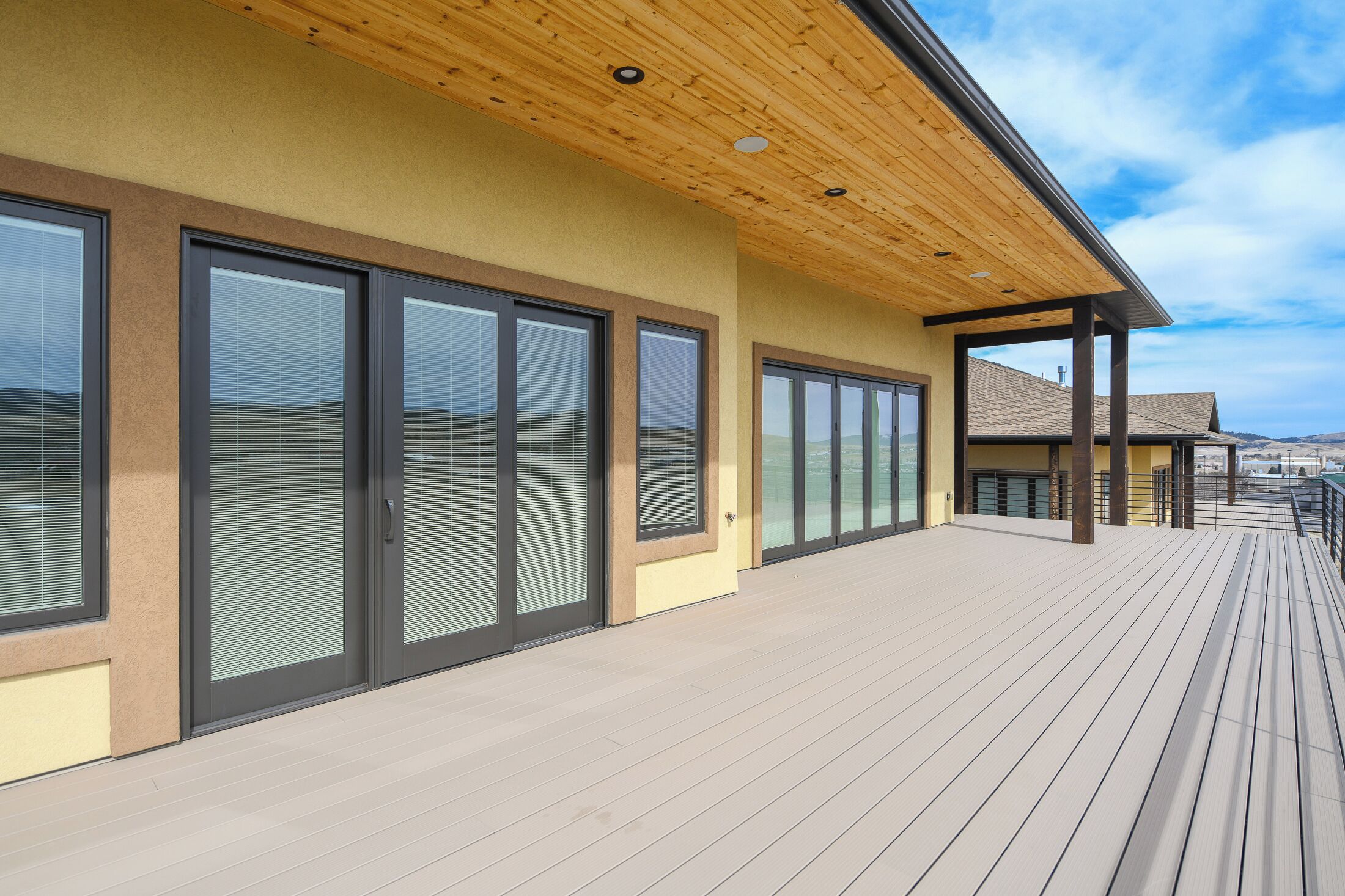 Een modern gebouw met grote schuifdeuren, een houten terras en een overdekt gebied met een schuin dak.