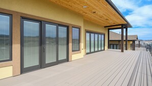 A modern building with large sliding glass doors, a wooden deck, and a covered area with a sloped roof. - Incredible Panoramic View, Close to Spearfish, Very Open Floor Plan & Paved! (Spearfish)