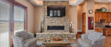 Una sala de estar con chimenea de piedra, dos sofás estampados, una mesa de centro y una gran pantalla de televisión.