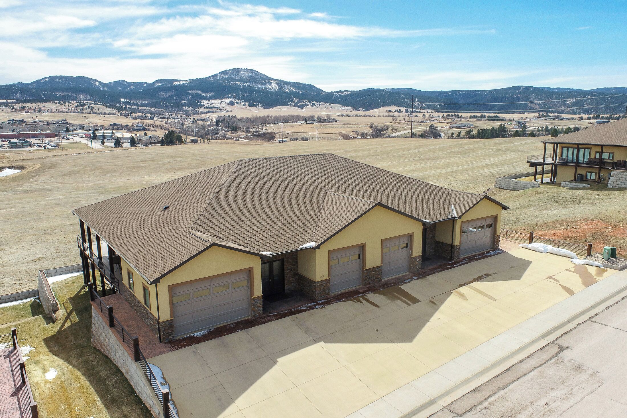 A large, single-story building with a flat roof and multiple garage doors, surrounded by open fields and distant mountains.