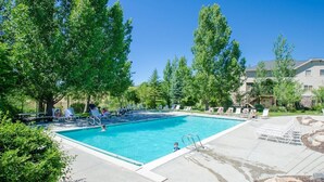 Una piscina rectangular rodeada de sillones de descanso y árboles, bajo un cielo azul despejado.