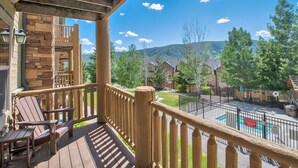 Terraza de madera con sillas Adirondack, un muro de piedra y vistas a una zona residencial con casas y árboles.