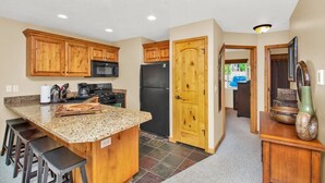 Una cocina con armarios de madera, encimera de granito, refrigerador negro y puerta de madera.