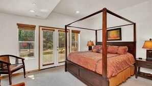 Una cama con dosel de madera, una mesita de noche con lámpara y una silla.