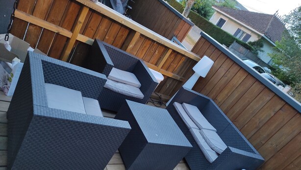A patio with a wooden deck, a large black and gray sectional sofa, and a white trash can. - Nice house in the center of Arès (Unknown)