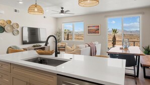 Een moderne keuken met een groot eiland, een eethoek met een tafel en stoelen, en uitzicht op het woestijnlandschap door grote ramen.