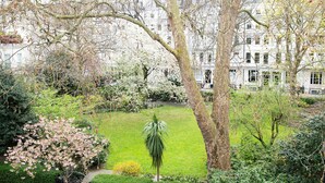 A garden with a lawn, trees, and a building in the background.