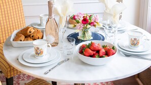 A breakfast setting with croissants, strawberries, a bottle of champagne, and a vase of flowers on a white table.