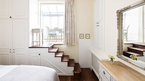 A bedroom with a bed, a dresser, a mirror, a window with curtains, and a staircase.