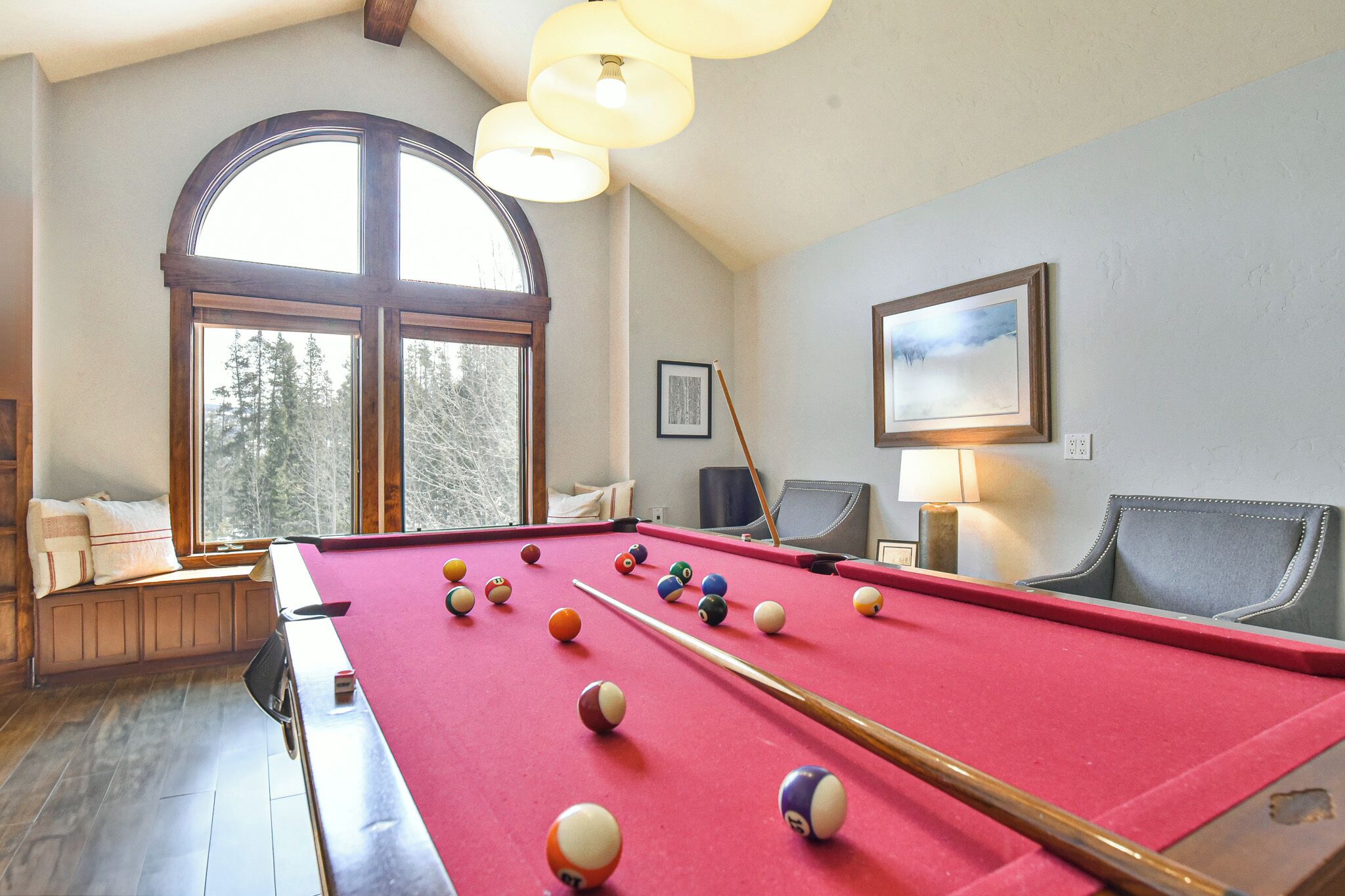 A pool table with balls, a window, and a chair.