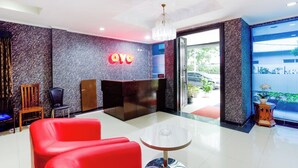 A hotel lobby with a reception desk, red seating, a chandelier, and a view of the outside. - Hotel O Bekasi Near Mall Lippo Cikarang Formerly Hotel Addictk (Cikarang)
