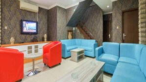 A modern living room with a blue sofa set, a red armchair, and a coffee table. A TV is mounted on the wall, and there is a staircase leading to another level. - Hotel O Bekasi Near Mall Lippo Cikarang Formerly Hotel Addictk (Cikarang)