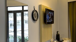 Hotelkamer met een grote spiegel, een hangklok, een televisie en een raam met uitzicht op een balkon.
