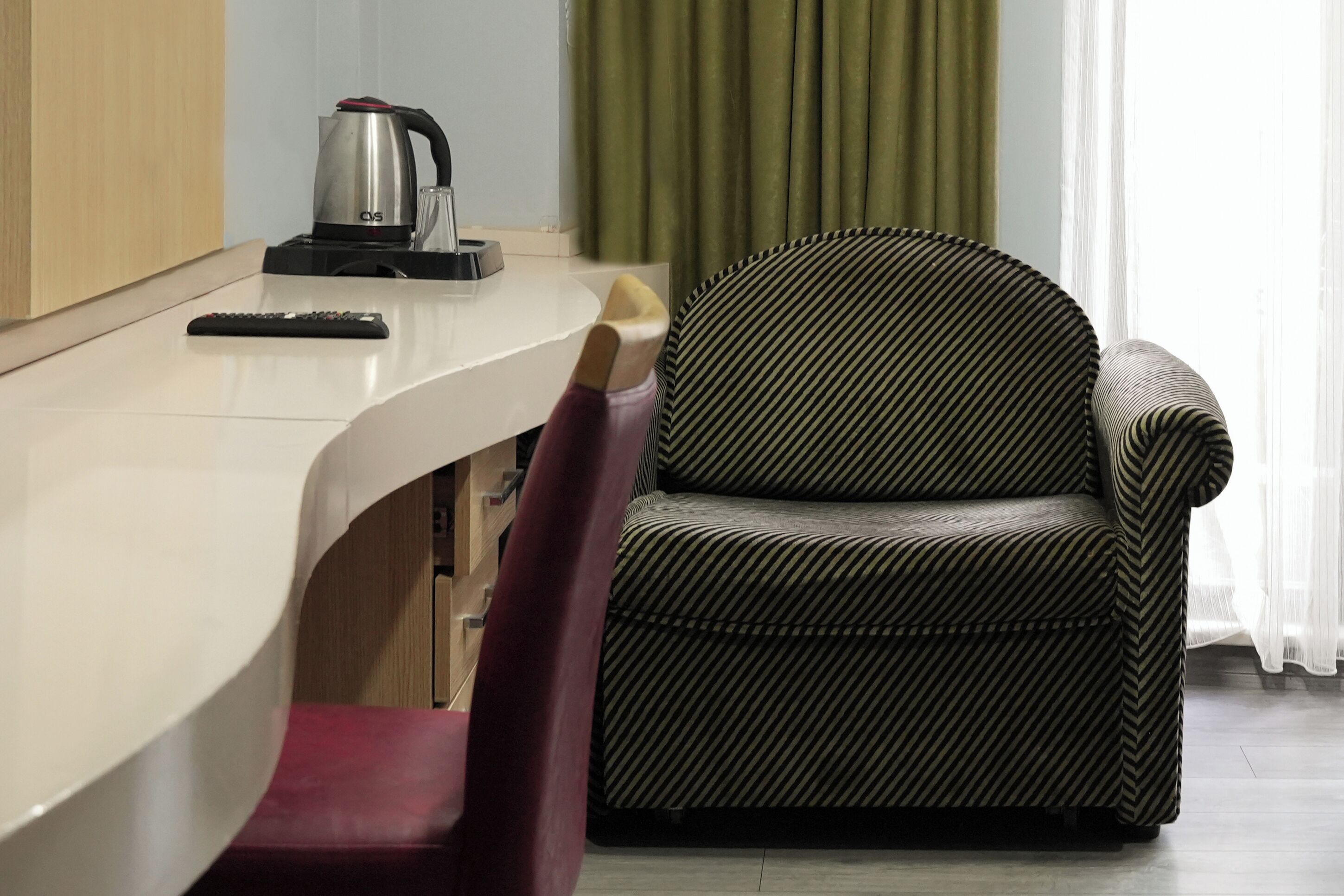 Une pièce moderne avec un bureau blanc aux lignes courbes, une chaise à rayures noires et blanches, une télécommande et une machine à café.