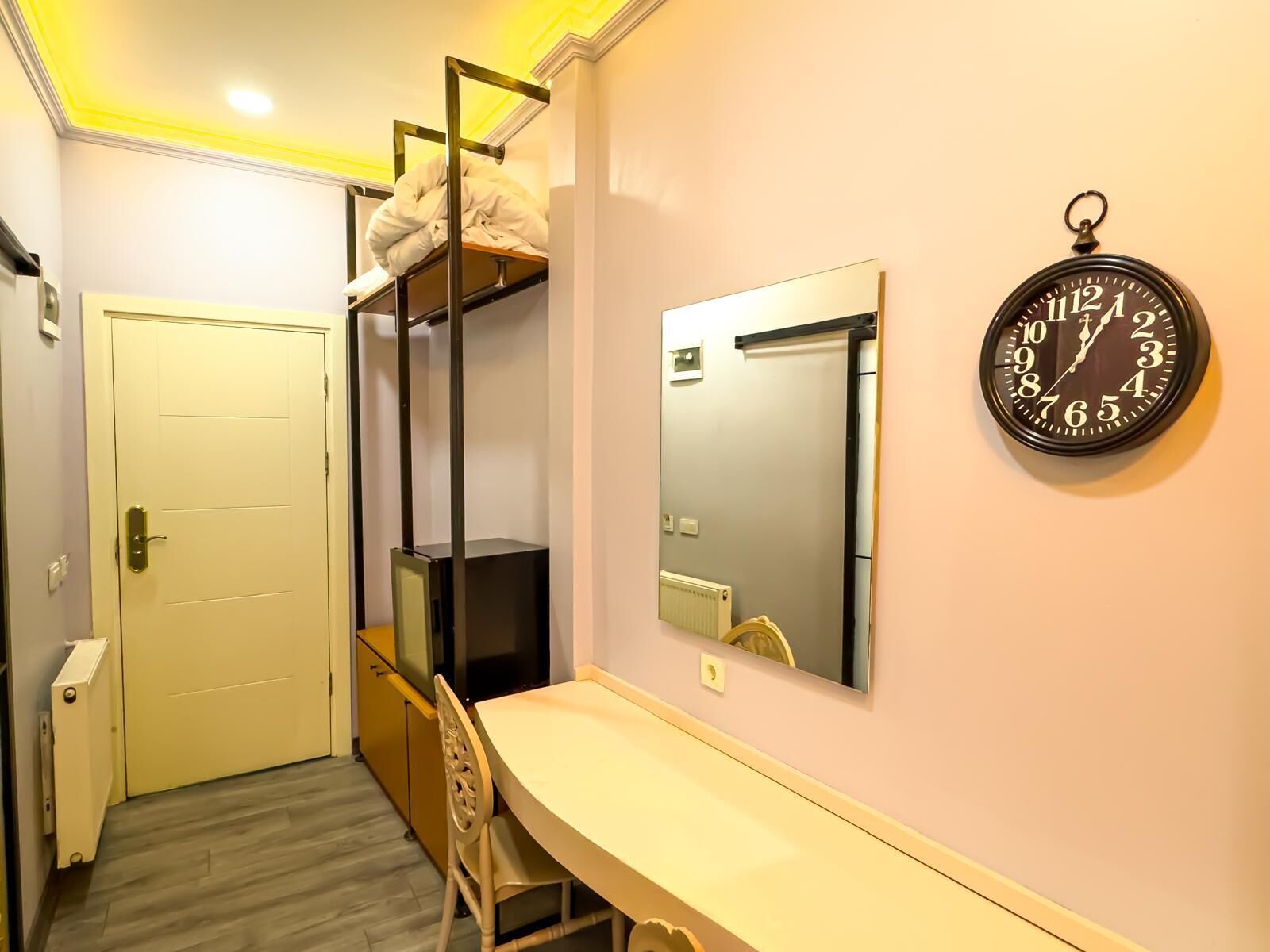 A compact room with a bunk bed, a desk, a chair, a mirror, and a wall clock.