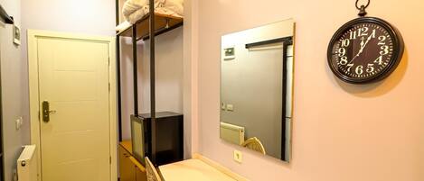 A compact room with a bunk bed, a desk, a chair, a mirror, and a wall clock.