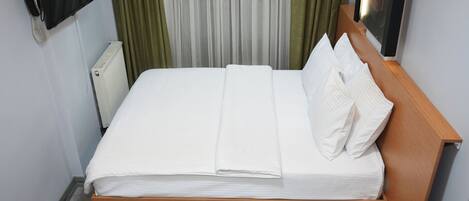 Un lit bien fait, avec du linge de lit blanc, une tête de lit en bois et une table de chevet sur laquelle se trouve une télécommande.