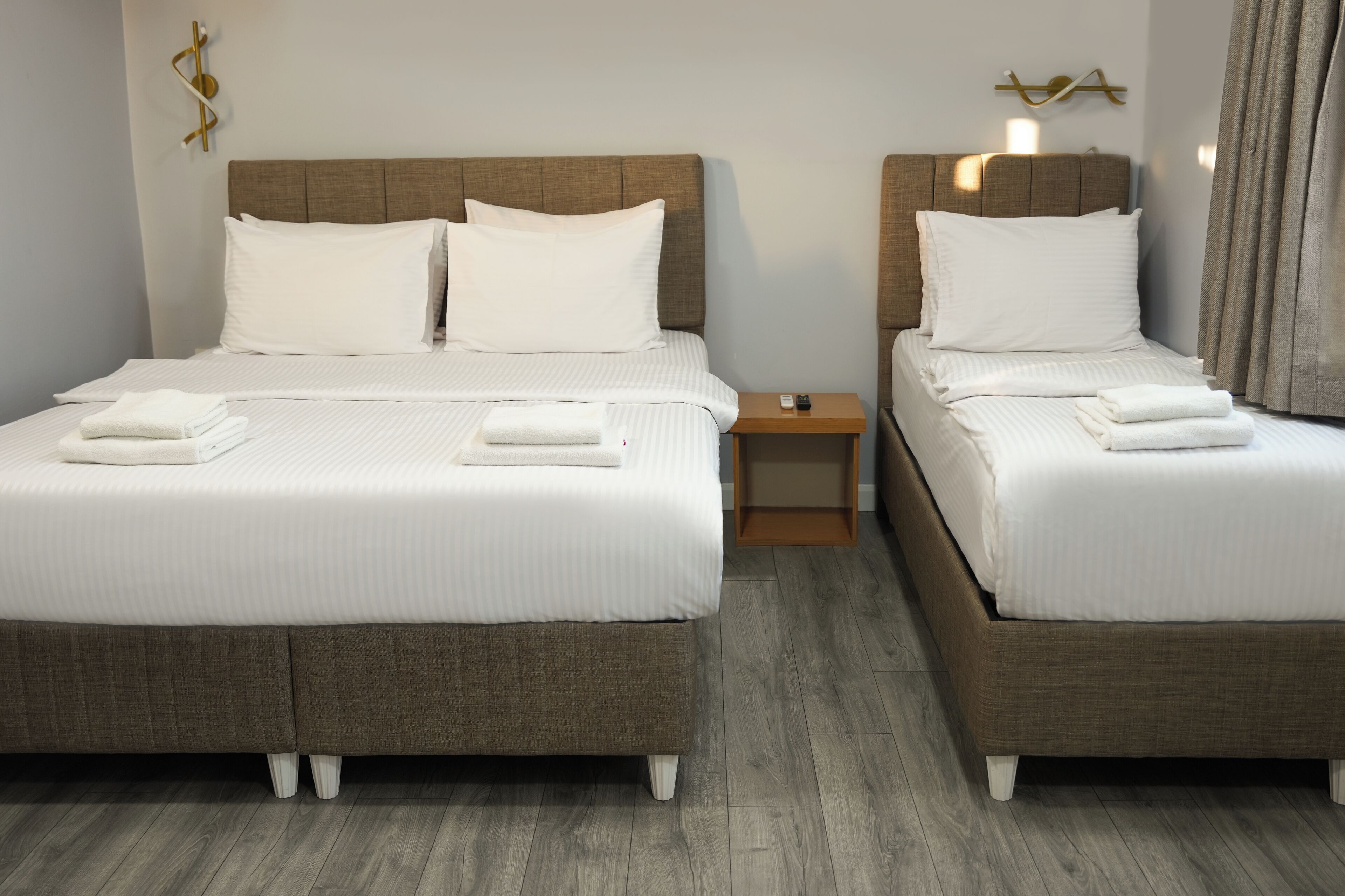 Two twin beds with white linens and pillows, a wooden nightstand, and a wall-mounted light fixture.