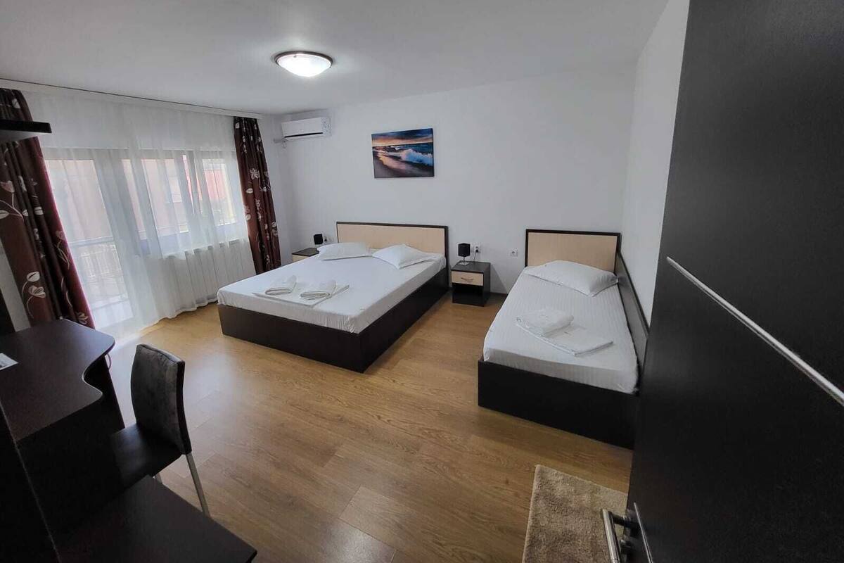 Habitación de hotel con dos camas, un escritorio y una silla. Hay un cuadro en la pared y un equipo de aire acondicionado.
