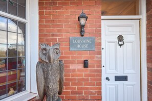 Een bakstenen muur met een bord waarop 'LOUVAINE HOUSE' staat en een witte deur met een deurbel.