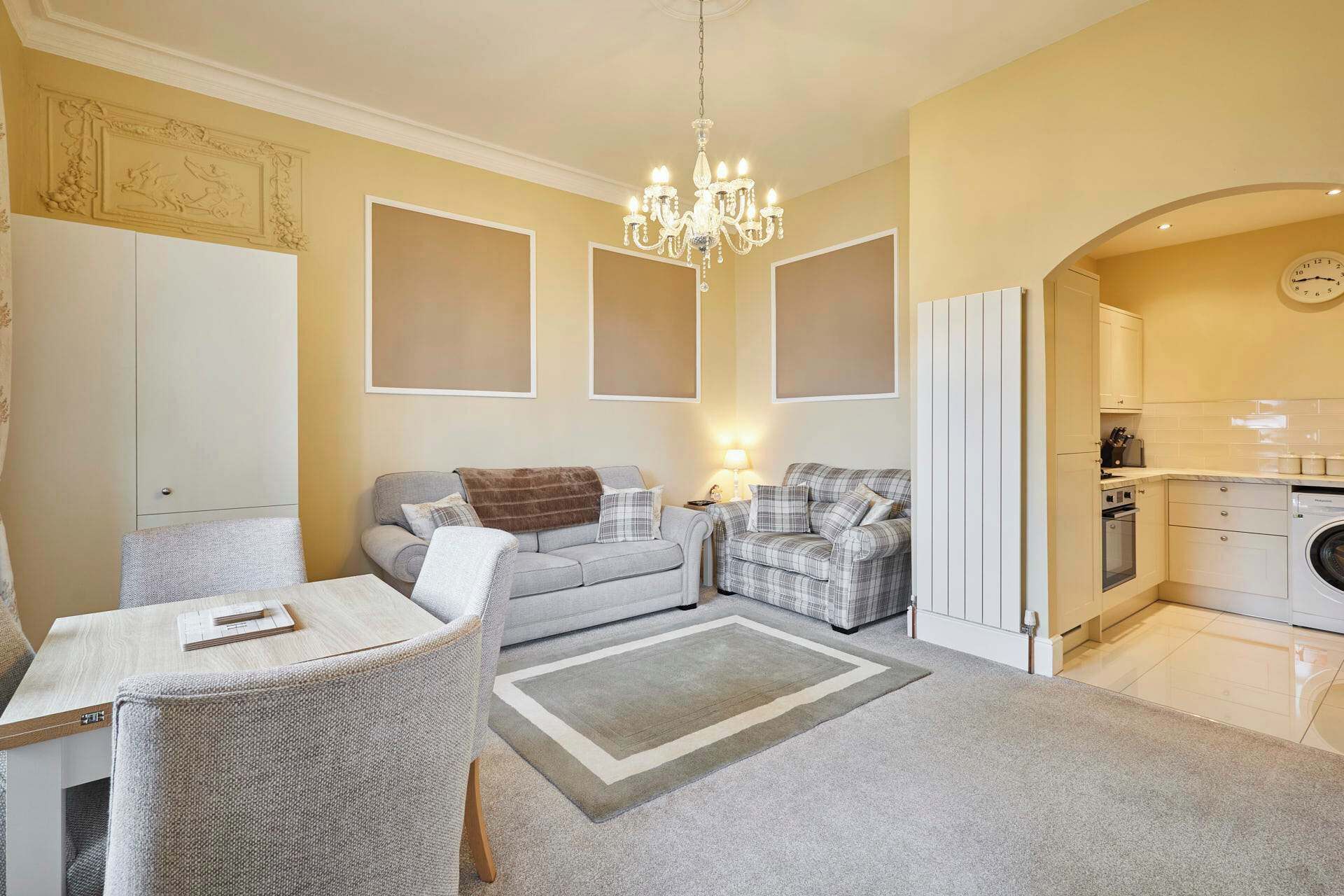 A living room with a dining area, a chandelier, and a kitchen visible through an archway.