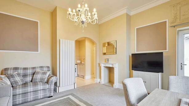 A living room with a sofa, a dining table, a chandelier, and a fireplace.
