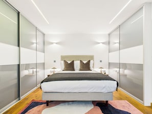 A modern bedroom with a large bed, glass walls, and recessed lighting.