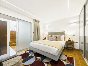 A modern bedroom with a large bed, a glass door leading to a balcony, and a patterned rug.