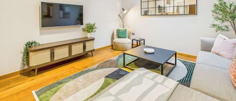 A modern living room with a flat-screen TV, a sofa, a coffee table, and a console table with plants.