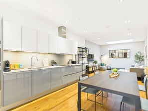 A modern kitchen with a central island, built-in appliances, and a dining area with a wooden table and chairs.