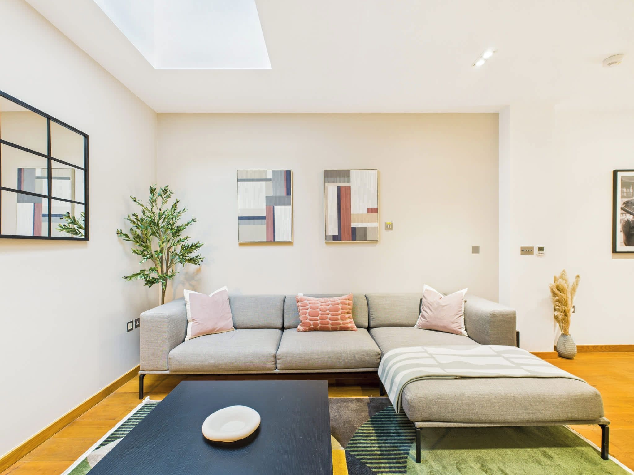A modern living room with a sectional sofa, a coffee table, and a small ottoman. There are abstract paintings on the walls and a potted plant.