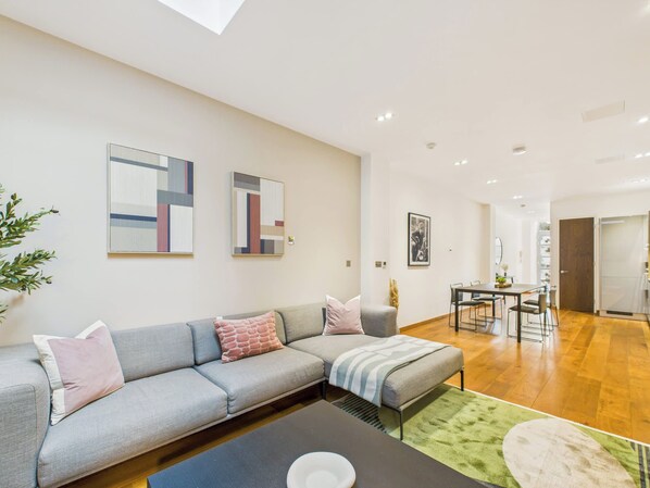 A modern living room with a grey sectional sofa, a coffee table, and a dining area with a table and chairs.