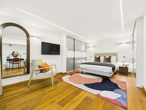 A modern bedroom with a large bed, a desk with a chair, a TV, and a sliding door closet.