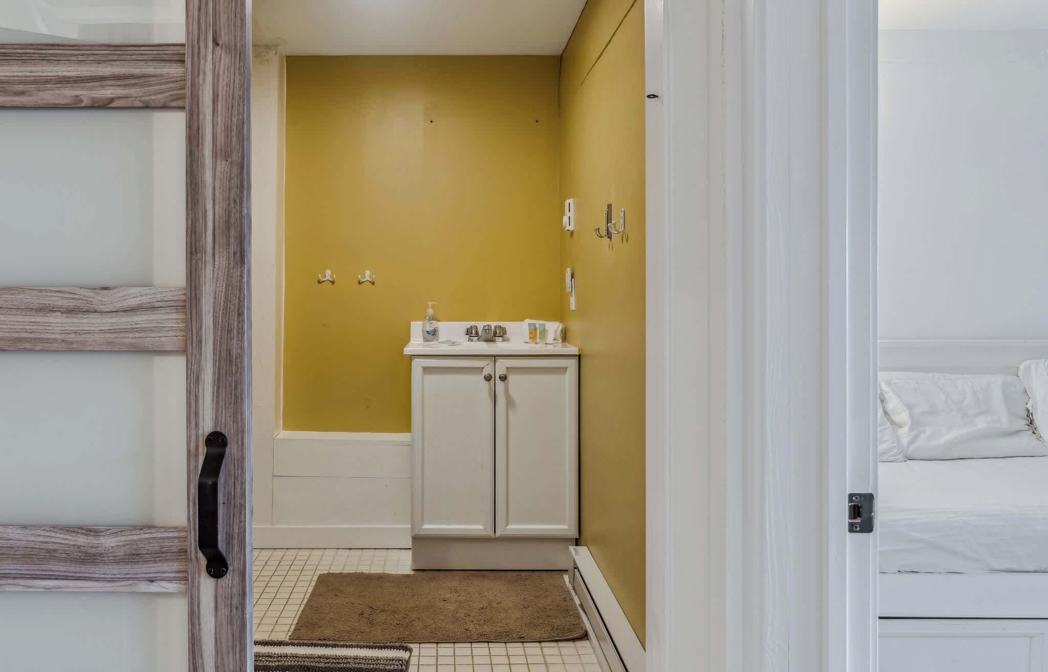 Un baño con una pared amarilla, un lavabo blanco y un armario blanco.