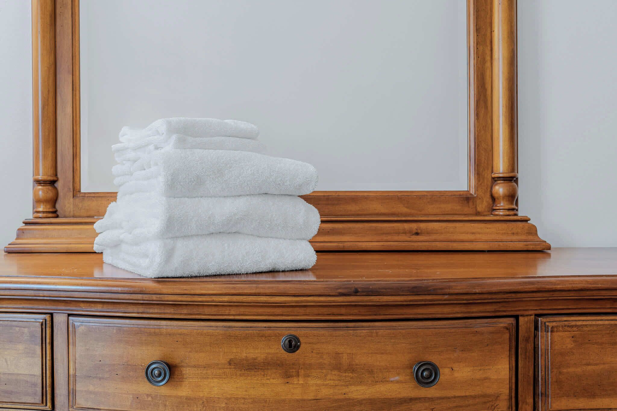 A stack of white towels on a wooden dresser with a mirror above.