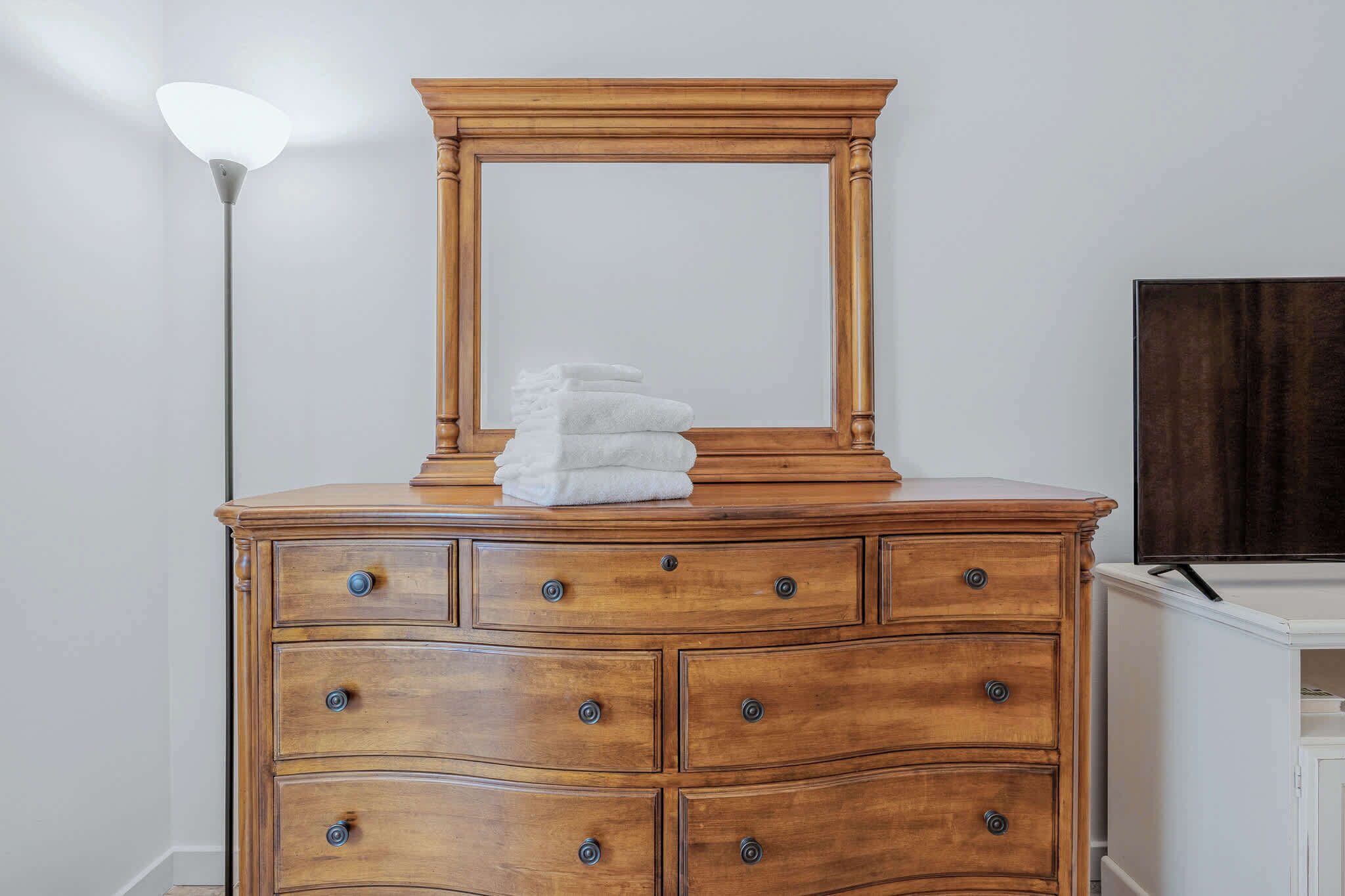 A wooden dresser with a mirror, drawers, and a stack of white towels.